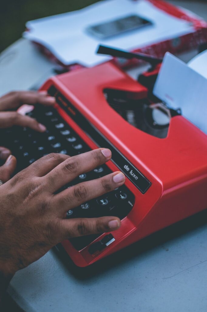 a red typewriter with someone's hands typing on it