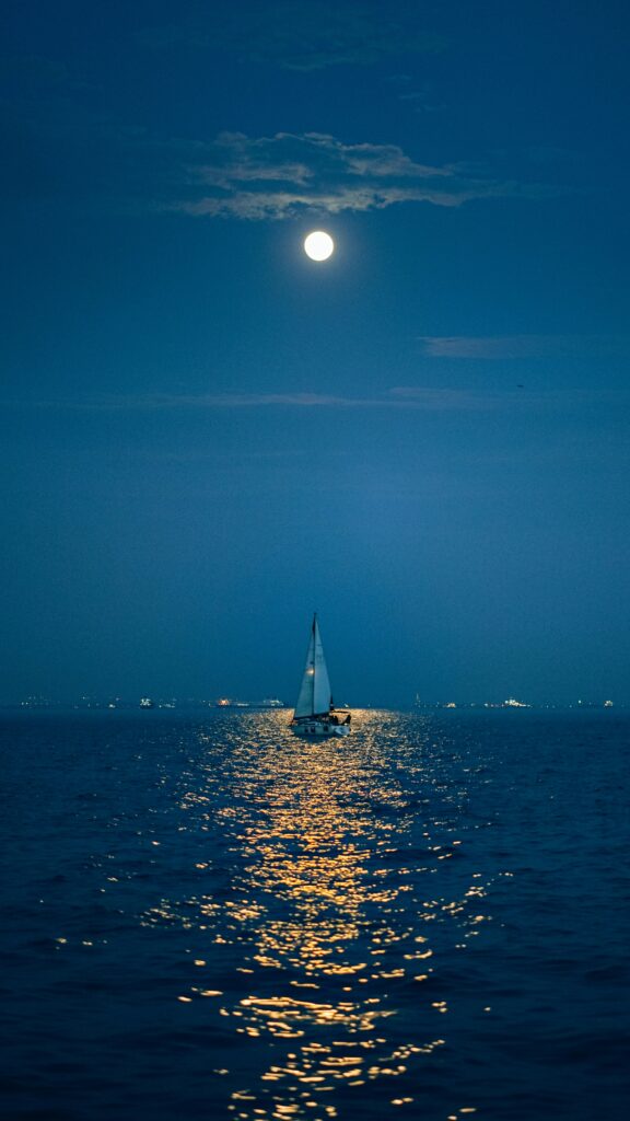 a boat in the ocean with a full moon above at night
