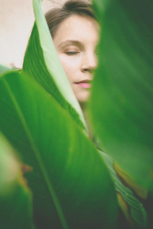 a women's face in between a close up of green plants